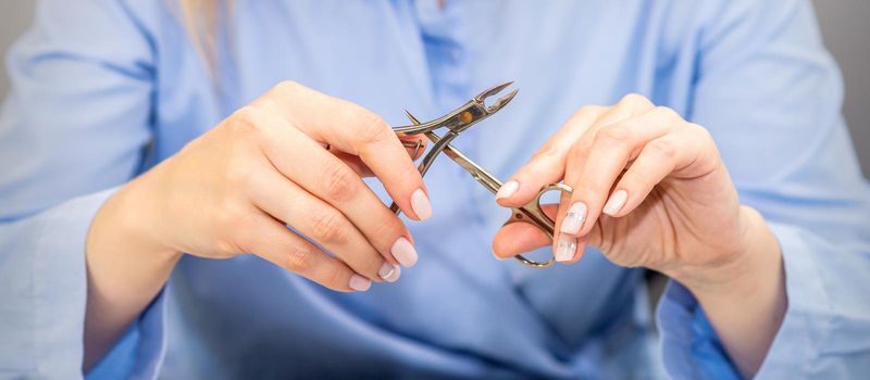 Hands of professional female manicurist holds manicure tools wearing blue workwear in beauty salon