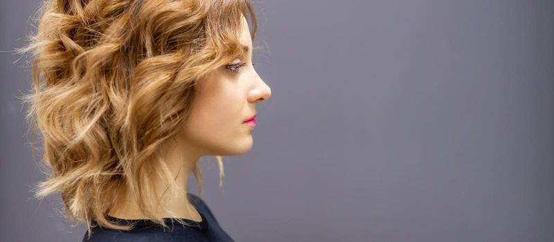 Side view portrait of the beautiful young caucasian woman with red long wavy hairstyle on dark gray background with empty space for text