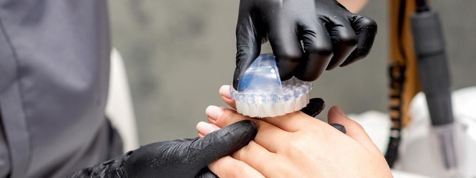 Manicure master is brushing dust from female fingernails in nail salon