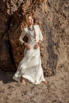 Middle aged woman looks good with blond hair, boho style in white long dress on the beach decorations on her neck and arms