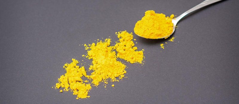 Turmeric or curcuma powder on metal spoon and scattered on dark background.