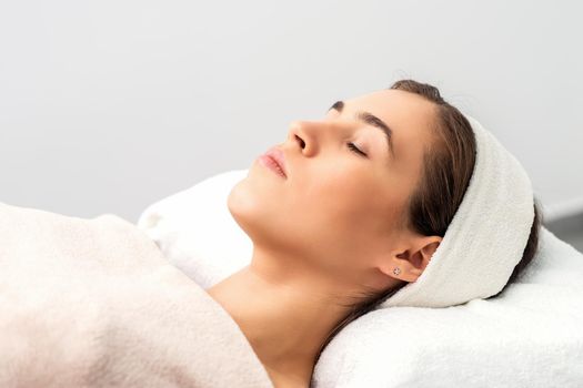 Side view of young woman lying on beautician table with closed eyes while waiting for cosmetic procedure in beauty salon