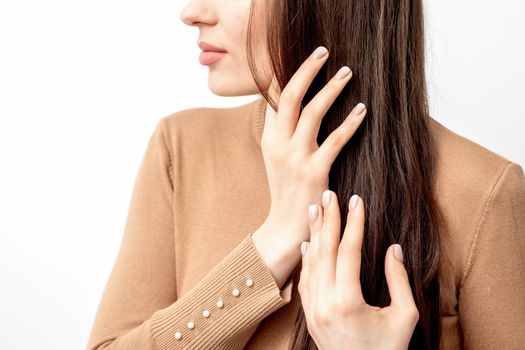 Side view portrait of beautiful young caucasian brunette woman touching her hair by manicured fingers on white background