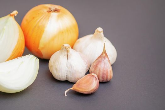 Unpeeled raw bulb and clove of garlic and onion on black surface with empty space for text