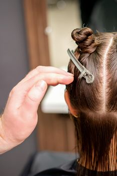 Rear view of hand of hairdresser doing haircut of young woman with hair clips on her hair in hair salon