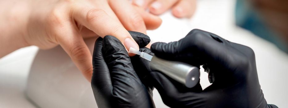 Manicure master is applying transparent varnish on female nails in nail salon