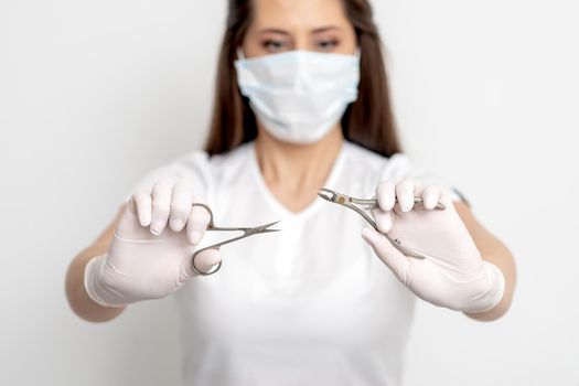 Manicure tools in hands of female manicurist wearing white mask and gloves on white background