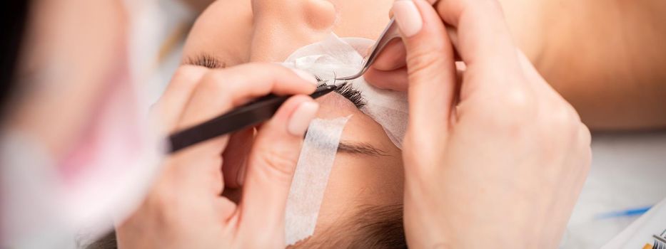 Young caucasian woman receiving eyelash extensions procedure in beauty salon