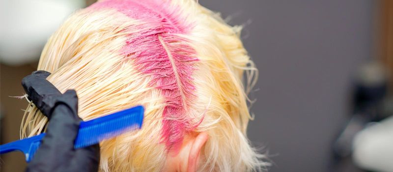 Hair coloring in pink color on hair roots of young blonde woman in hair salon. Selective focus