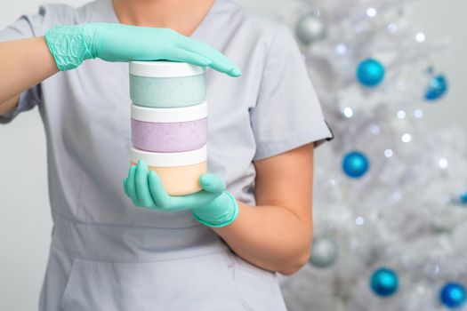 Female cosmetologist holding three blank jars with sugaring paste on christmas tree background