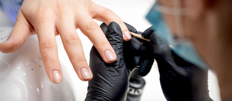 Closeup of manicurist removes cuticles on female nails by wooden orange stick in nail salon