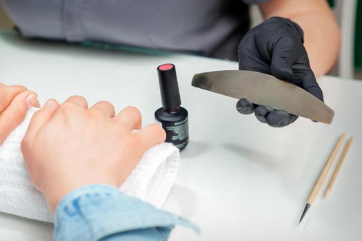 Female hands prepares to procedure by nail file in hands of manicurist in nail salon