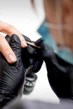 Closeup of manicurist removes cuticles on female nails by wooden orange stick in nail salon