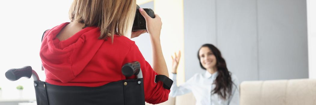 Portrait of professional photographer take pictures of pretty model posing on sofa. Creative artist with photocamera in wheelchair. Disabled people concept