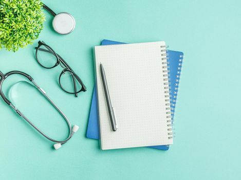 Open notebook with a pen and glasses on a green hospital background flat lay. top view. Nurse workplace concept. Stethoscope on the doctor work desk.