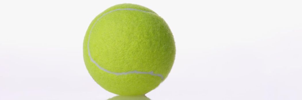 Close-up of single yellow round tennis ball sport equipment placed on reflecting surface. Sport, competition, game concept. Copy space, white background