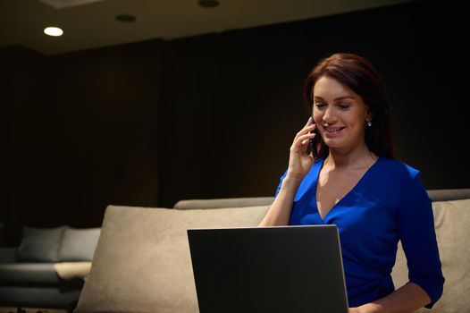 Portrait of successful Caucasian middle-aged pretty woman interior designer using laptop computer and internet, talking on mobile phone. Multitasking female entrepreneur. Successful business concept.
