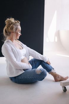 Close up portrait of pregnant woman in studio on white background. Beautiful future mother put her her hands on her belly. Stylish woman in white jaket