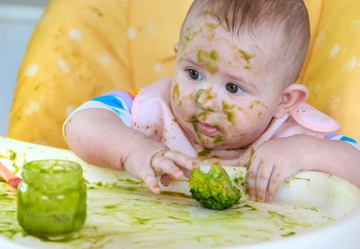 Little baby eats broccoli puree himself. Selective focus. People.