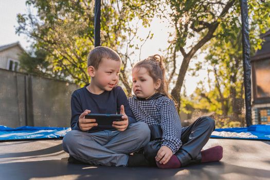 children sit on a trampoline and look at the phone