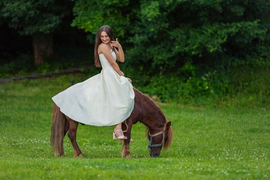 girl in a white dress rides a pony on a green lawn
