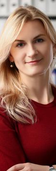 Portrait of presentable office worker smiling and posing for photo with crossed arms. Young woman in red sweater on folder background. Office life concept