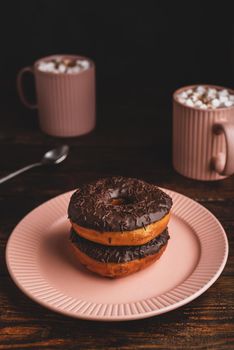 Stack of Homemade Chocolate Donuts and Mugs of Hot Chocolate with Marshmallow on Rustic Wooden Surface