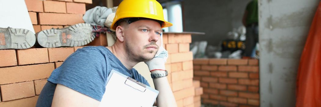 Portrait of upset worker sit surrounded with construction site mess with paper. No candidates to invest in buildings. Building complex, real estate concept