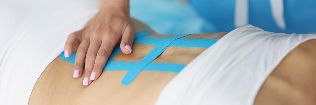 Close-up of doctor holding x ray of womans back and correct kinesiology tape. Procedure on recovering after injury. Rehabilitation room, healthcare concept