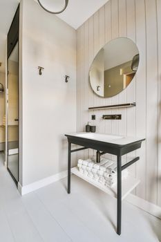 A large round mirror and a small sink next to a wardrobe with a mirrored door in a bright room