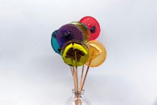 Colored lollipops with different berries and fruits inside in a bottle on a white background.