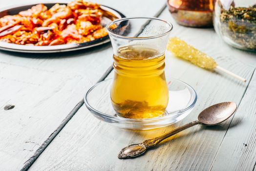 Herbal tea in armudu glass with arabic delights on metal plate over light wooden surface