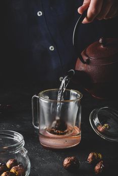 Steeping red tea in glass mug. Pouring boiled water from iron kettle.
