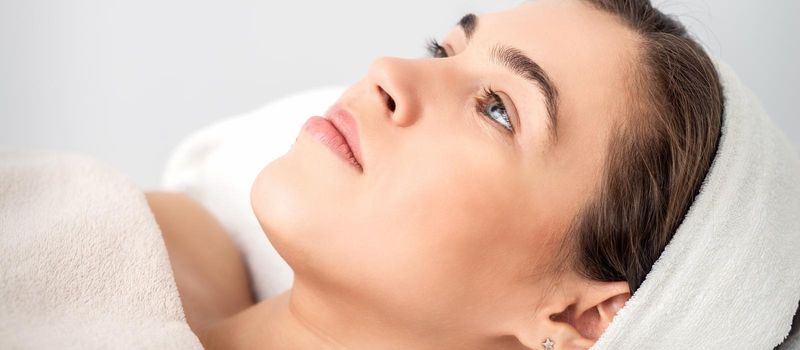 Side view portrait of pensive young woman lying on beautician table while waiting for cosmetic procedure in beauty salon