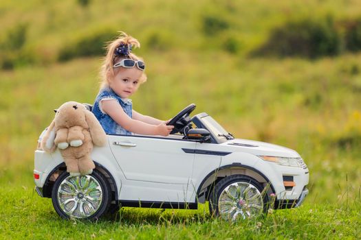 little girl rides on a children's car on a green lawn