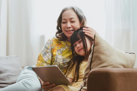 Happy moments of Grandmother and Granddaughter watching media on digital tablet at home. Family concept