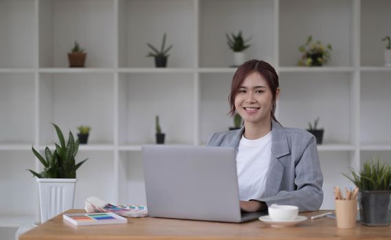 Beautiful smiling young graphic designer sitting at desk in office and working.