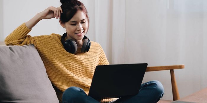 Cheerful freelancer working on laptop sitting on couch and listening to music in headphones, copyspace