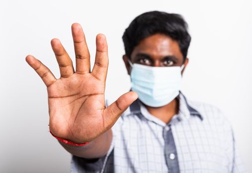 Closeup Asian handsome black man wearing surgical hygienic protective cloth face mask against coronavirus and raising hand stop sign, studio shot isolated white background, COVID-19 medical concept