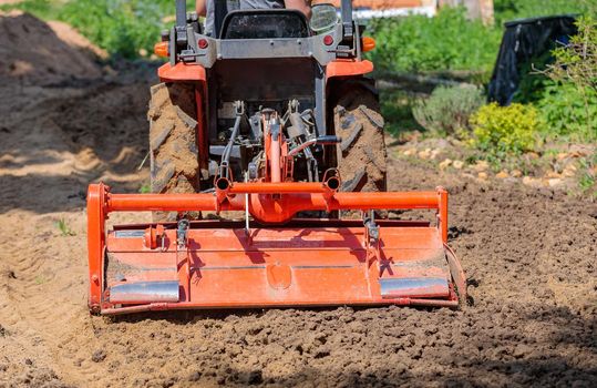 A farmer on a mini tractor loosens the soil for the lawn. Land cultivation, surface leveling.