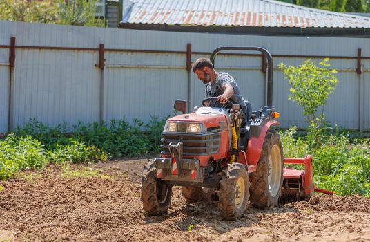 A farmer on a mini tractor loosens the soil for the lawn. Land cultivation, surface leveling.