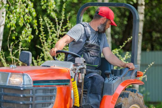 A farmer on a mini tractor loosens the soil for the lawn. Land cultivation, surface leveling.