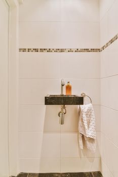 Black sink with soap, towel, shiny faucet in a bright room, with a dark tiled floor