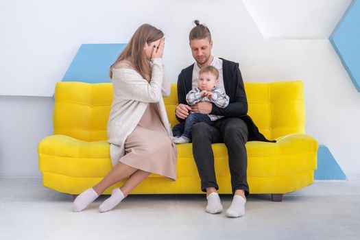 Young caucasian happy family with his little kid having fun on sofa in bright interior.