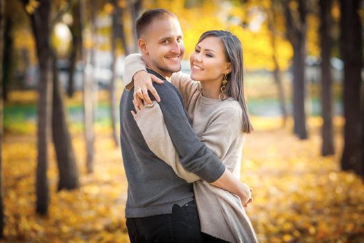 Young international couple hugging on a date in autumn city park.