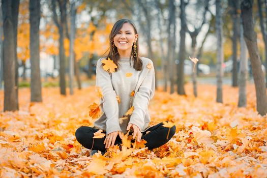 Happy mixed race fall young woman smiling joyful covered with autumn leaves outside in fall forest.