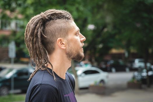 Profile portrait of a caucasian man with dreadlocks, beard and sidecut on a summer outdoor.