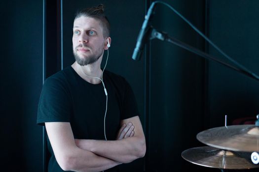 Portrait of a caucasian drummer in a black room of a recording studio behind a drum kit.