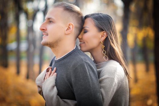 Young woman hugging her man from behind, man looks into the distance.