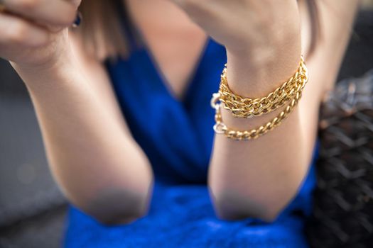 Bracelet in the form of a chain on the wrist of a woman in a blue dress.